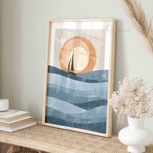 May include: A framed print of a sailboat sailing on blue waves with a large orange sun in the background. The print is in a wooden frame and is hanging on a wall.