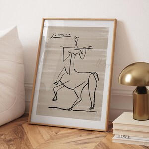 Op de afbeelding: Een ingelijste print van een zwart-witte lijntekening van een centaur op een beige achtergrond. De handtekening van de kunstenaar is zichtbaar in de linkerbovenhoek van de print.