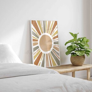 May include: A framed print of a stylized sun with rays in shades of brown, yellow, and gray. The sun is on a white background.