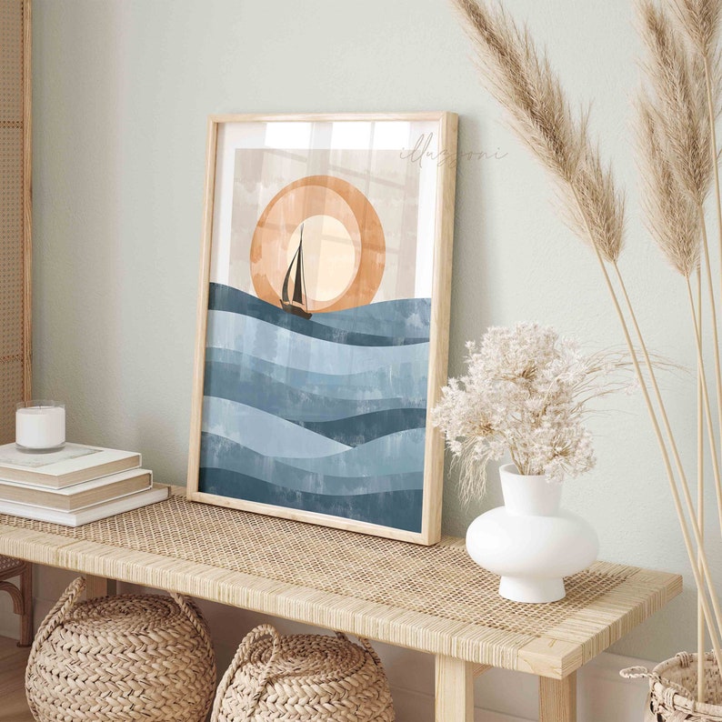 May include: A framed print of a sailboat sailing on blue waves with a large orange sun in the background. The print is in a wooden frame and is hanging on a wall.