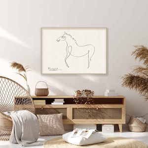 May include: A black and white line drawing of a horse by Pablo Picasso, framed in a light wood frame, hanging on a white wall above a light wood cabinet with a wicker chair and a woven rug.