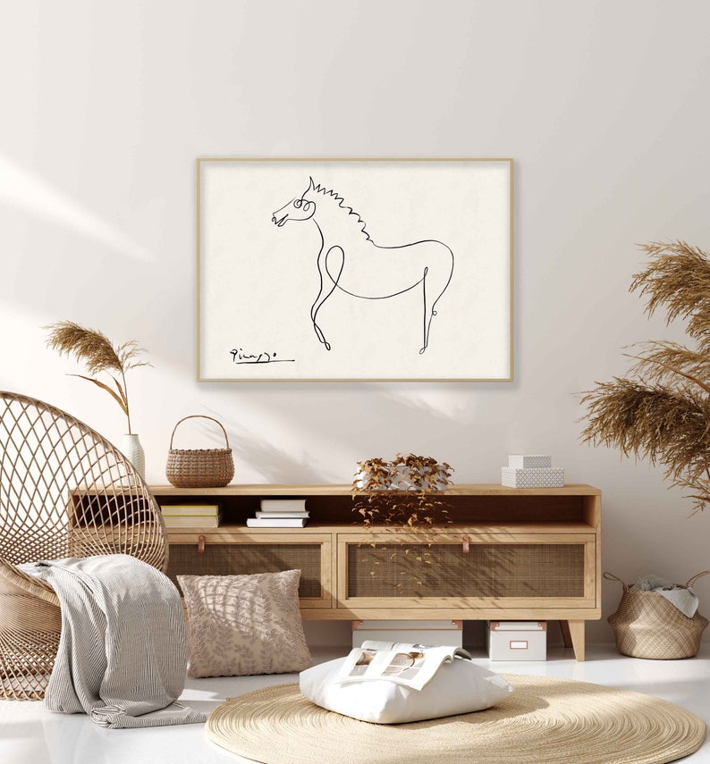May include: A black and white line drawing of a horse by Pablo Picasso, framed in a light wood frame, hanging on a white wall above a light wood cabinet with a wicker chair and a woven rug.