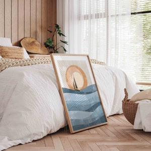 May include: A framed print of a minimalist abstract art design featuring a sailboat on a blue and white ocean with a large orange sun in the background.