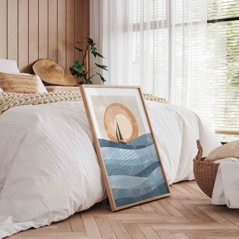 May include: A framed print of a minimalist abstract art design featuring a sailboat on a blue and white ocean with a large orange sun in the background.