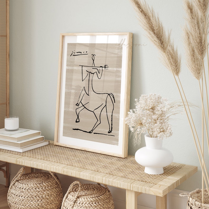 Op de afbeelding: Een ingelijst zwart-wit lijntekening van een persoon die een paard berijdt. De tekening is op een beige achtergrond met een textuur. De lijst is van hout en heeft een lichtbruine afwerking.