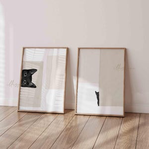 May include: Two framed prints with abstract geometric shapes in beige and white. One print features a black cat peeking from behind a shape, while the other print shows a black cat standing behind a shape.