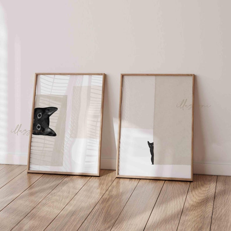 May include: Two framed prints with abstract geometric shapes in beige and white. One print features a black cat peeking from behind a shape, while the other print shows a black cat standing behind a shape.