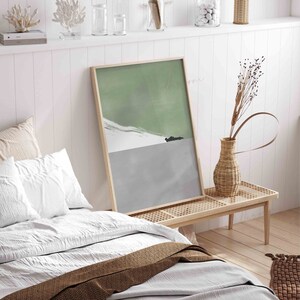 Puede incluir: Una impresi&oacute;n de arte abstracto enmarcada con un esquema de color verde y gris. La impresi&oacute;n presenta un paisaje estilizado con una silueta de coche en la distancia. La impresi&oacute;n est&aacute; colgada en una pared blanca sobre un banco de madera.