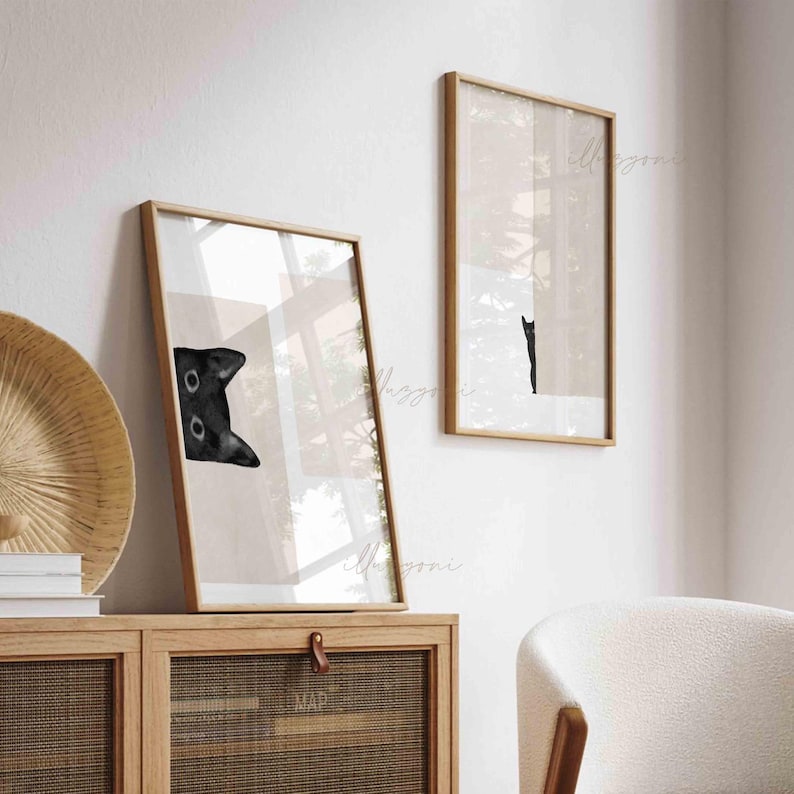 May include: Two framed black and white illustrations of cats. One image shows a cat peeking from behind a wall, while the other shows a cat walking away from the viewer.