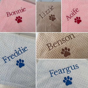 Pode incluir: Uma cole&ccedil;&atilde;o de mantas macias com textura de waffle em rosa, bege e azul claro. Cada manta apresenta um nome bordado, incluindo Bonnie, Lizzie, Aoife, Freddie, Benson e Feargus, acompanhado por uma pegada de pata costurada.