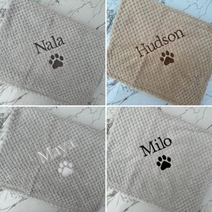 Pode incluir: Uma cole&ccedil;&atilde;o de quatro mantas com textura de tecido waffle em cinza e bege. Cada manta apresenta um bordado personalizado com um nome e um &iacute;cone de pata. Os nomes exibidos s&atilde;o Nala, Hudson, Maya e Milo, costurados em v&aacute;rias cores de linha.