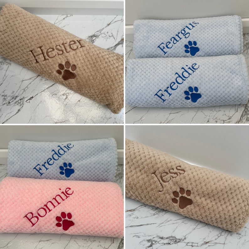 Pode incluir: Uma cole&ccedil;&atilde;o de mantas macias e texturizadas em tons de bege, azul claro e rosa. Cada manta apresenta nomes bordados como Hester, Feargus, Freddie, Bonnie e Jess, acompanhados por um &iacute;cone de pata costurado na mesma cor.