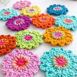 Könnte beinhalten: Eine Sammlung farbenfroher, gehäkelter Untersetzer in Blumenform. Jeder Untersetzer hat eine lebendige Farbpalette, darunter Rosa, Orange, Gelb, Grün und Blau, mit einem kontrastierenden Zentrum. Die handgefertigten Untersetzer sind auf einer weißen Oberfläche angeordnet.