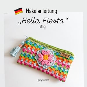 Op de afbeelding: Een rechthoekig gehaakt tasje met een veelkleurig ruitpatroon in oranje, roze, groen en blauw. Een lichtblauwe en roze gehaakte bloemapplicatie is in het midden aan de voorzijde bevestigd. Het heeft een groene rits, een lichtblauw kwastje en een klein bruin label met de tekst MYNICOSCH. Tekst: Häkelanleitung Bella Fiesta Bag @mynicosch.