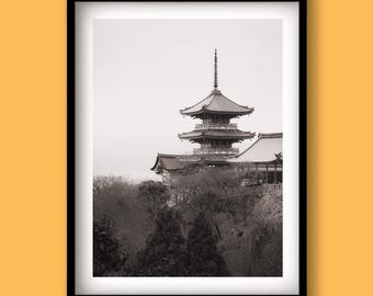 May include: Black and white photograph of a Japanese pagoda framed in a black border. The multi-tiered structure is set against a cloudy sky, with trees in the foreground. The image evokes a sense of tranquility and cultural heritage.