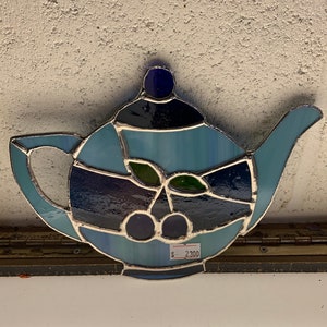 Könnte beinhalten: Eine Bleiglas-Teekanne mit blauem und grünem Design. Die Teekanne hat ein Kirschmotiv mit grünen Blättern. Das Preisschild zeigt 2300 €.