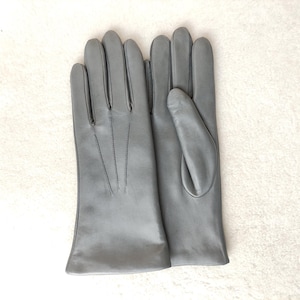 Peut inclure: Une paire de gants en cuir gris mat et lisse. Le gant gauche montre le dos avec trois lignes de couture verticales partant des doigts vers le poignet, tandis que le gant droit pr&eacute;sente le c&ocirc;t&eacute; paume avec une section pour le pouce.