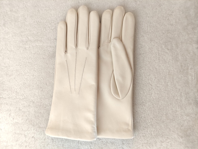 Peut inclure: Une paire de gants en cuir de couleur cr&egrave;me avec une finition lisse et trois lignes de couture d&eacute;coratives verticales sur le dos de la main. Les gants pr&eacute;sentent une coupe classique avec une ouverture droite au poignet et des doigts s&eacute;par&eacute;s.