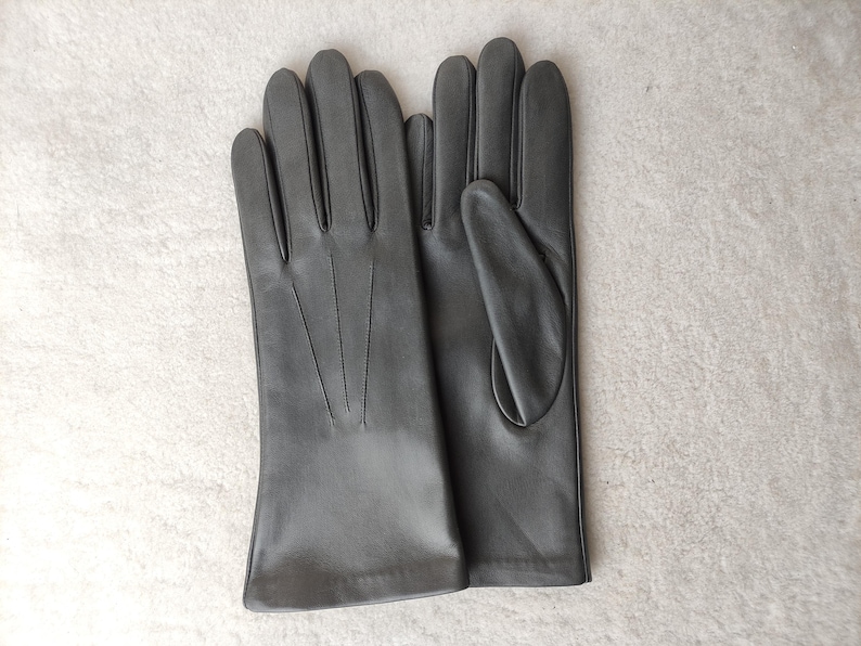 Peut inclure: Une paire de gants en cuir noir avec une finition lisse et trois lignes de couture d&eacute;coratives verticales sur le dos de la main. Les gants pr&eacute;sentent une coupe classique avec une ouverture droite au poignet et un pouce s&eacute;par&eacute;.