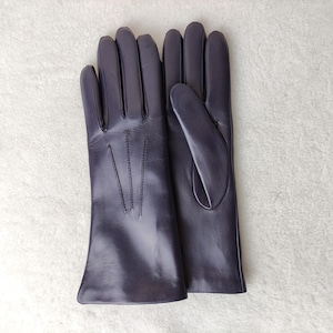 Peut inclure: Une paire de gants en cuir violet fonc&eacute; avec une finition lisse, quatre doigts et un pouce. Le dos du gant gauche pr&eacute;sente trois lignes de couture verticales s'&eacute;tendant de la base des doigts vers la zone du poignet.