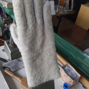 May include: A white, fluffy glove with a leather palm and white stitching. The glove is made of a soft, textured material and appears to be new. The glove is designed to fit a right hand.