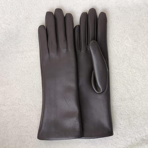 May include: A pair of dark brown gloves with a smooth, matte finish. The gloves feature a classic design with four fingers and a thumb section, extending to the wrist. The material appears uniform in color and texture throughout the surface.