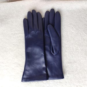 May include: A pair of dark purple leather gloves with a smooth finish. The gloves feature a classic design with four fingers and a thumb, extending past the wrist. The leather has a subtle sheen and visible natural grain texture throughout.
