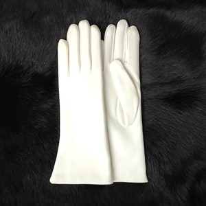 May include: A pair of solid white gloves with a smooth, matte finish. The gloves feature a classic design with four fingers and a thumb, extending past the wrist with a slightly flared opening at the cuff, showcasing clean, stitched seams.