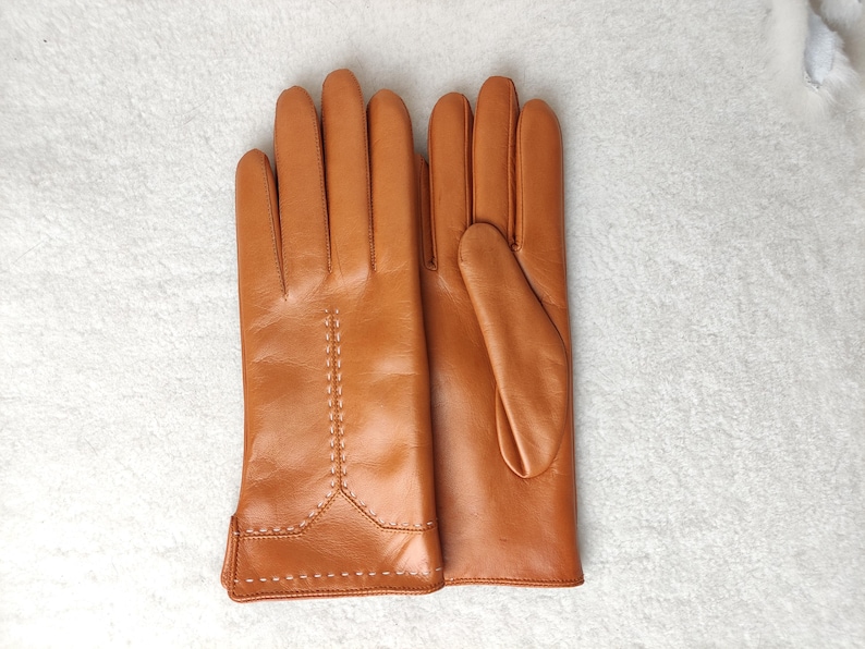 Puede incluir: Un par de guantes de cuero color canela. Los guantes est&aacute;n hechos de cuero liso y presentan costuras decorativas a lo largo de las costuras. Los guantes est&aacute;n dise&ntilde;ados para un ajuste c&oacute;modo y son adecuados para el clima fr&iacute;o.