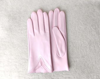 May include: A pair of light pink leather gloves featuring a V-shaped cuff detail with intricate scalloped edges and small perforated holes along the wrist opening. The gloves have a smooth finish and are designed with four fingers and a thumb.