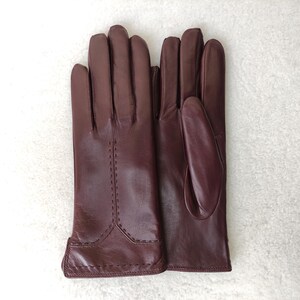 Puede incluir: Un par de guantes de cuero burdeos. Los guantes est&aacute;n hechos de cuero liso y presentan costuras decorativas a lo largo de las costuras. Los guantes est&aacute;n dise&ntilde;ados para ajustarse a la mano.