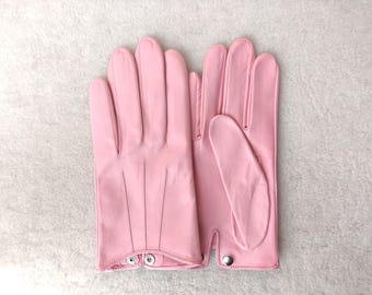 May include: A pair of light pink leather gloves featuring three decorative stitched lines on the back of the hand and a small silver-toned metal snap button closure at the wrist. The gloves have a smooth finish and a classic five-finger design.