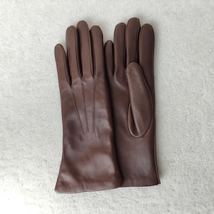 Peut inclure: Une paire de gants en cuir marron lisse pr&eacute;sentant trois lignes verticales cousues sur le dos de la main. Les gants ont une coupe classique avec une ouverture droite au poignet et un pouce positionn&eacute; sur le c&ocirc;t&eacute; du gant droit.