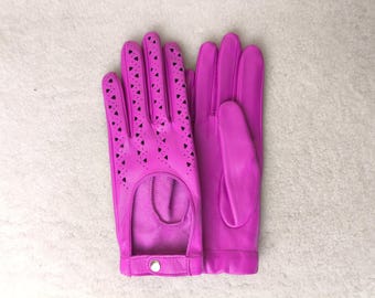 May include: A pair of vibrant fuchsia gloves featuring a cutout design on the back of the hand and fingers. The gloves are adorned with small triangular perforations along the fingers and include a wrist strap with a single silver snap button.