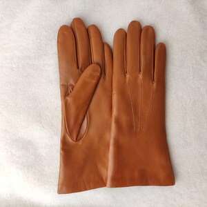 Peut inclure: Une paire de gants en cuir marron clair avec une finition lisse, quatre doigts et un pouce. Le dos du gant droit pr&eacute;sente trois lignes de couture verticales s'&eacute;tendant de la base des doigts vers la zone du poignet.