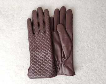 May include: A pair of dark brown gloves. The left glove features a quilted diamond pattern on the back, while the right glove has a smooth palm side with a gathered elastic wrist detail. Both gloves are constructed with five fingers.
