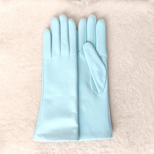 May include: A pair of light blue opera-length gloves made of a smooth, matte material. The gloves feature a classic design with four fingers and a thumb, extending past the wrist to the mid-forearm, showcasing a clean and uniform finish.