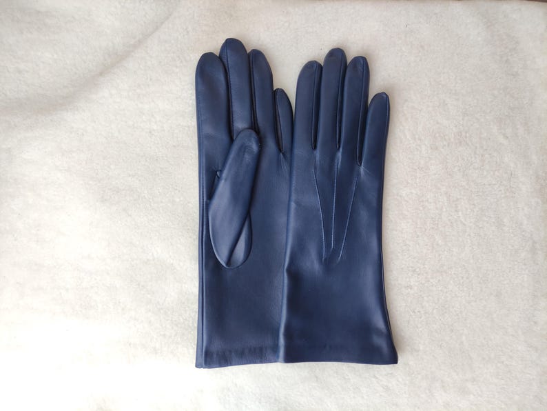 Peut inclure: Une paire de gants en cuir bleu marine avec une finition lisse, quatre doigts et un pouce. Le dos du gant droit pr&eacute;sente trois lignes verticales cousues s'&eacute;tendant du poignet vers les articulations pour plus de d&eacute;tails.