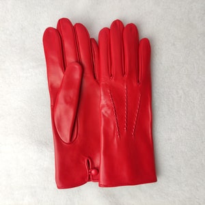 May include: A pair of vibrant red leather gloves featuring a smooth finish, four fingers and a thumb on each hand, decorative stitching on the back of the hand, and a small button closure detail at the wrist opening for a secure fit.