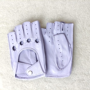 Puede incluir: Un par de guantes de cuero sin dedos en color lavanda claro con detalles perforados en los dedos y el dorso de la mano. Los guantes incluyen un diseño recortado en la palma y un pequeño cierre de botón a presión de tono plateado en la muñeca.