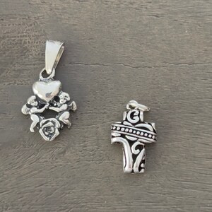Peut inclure: Deux pendentifs en argent, l'un représentant un cœur tenu par deux chérubins avec une rose en dessous, et l'autre une croix détaillée avec une bordure décorative.