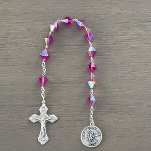 Könnte beinhalten: Ein silbernes Rosenkranz mit einem silbernen Kruzifix und einer silbernen Sankt-Michaels-Medaille. Die Rosenkranzkugeln sind aus rosafarbenem, irisierendem Glas.