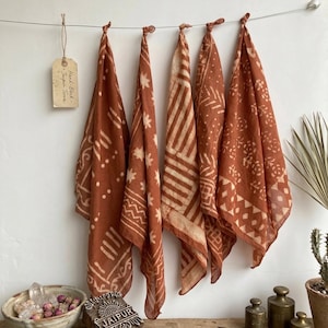 Peut inclure: Cinq textiles roux à motifs crème sont suspendus à un fil. Chaque textile présente un motif différent. Une étiquette indique "Hand-Block - Jaipur Terra". Un bloc de bois avec "JAIPUR" est sur une surface en bois.