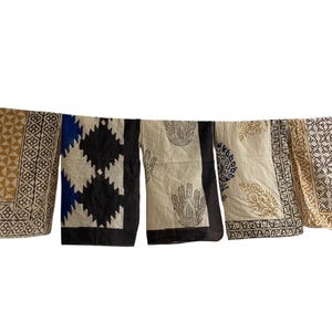 May include: Several patterned textiles hanging on a washing line. The textiles display geometric, paisley, and hand-print designs in tan, black, blue, and cream. The rectangular textiles appear to be made of fabric, with a variety of patterns.
