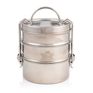 Peut inclure: Une boîte à lunch en acier inoxydable argentée à trois étages avec une poignée de transport et des loquets. La boîte à lunch porte l'inscription "Indian Tiffin" gravée sur le côté.