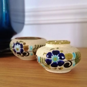 Könnte beinhalten: Zwei kleine, runde Keramik-Töpfe mit einer gesprenkelten weißen Glasur. Die Töpfe sind mit blauen, grünen und braunen Blumendesigns verziert.