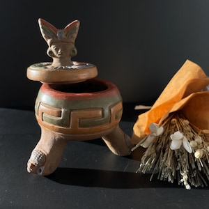 以下が含まれることがあります： 蝶の羽根を持つ彫刻された女性の顔が付いた蓋が付いた、小さなセラミック製の亀の形をした宝箱。箱は緑、茶色、赤の塗料で装飾されており、3本の脚があります。