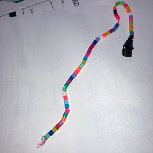 May include: A colorful beaded string with a black plastic end piece. The string is made of small, round beads in various colors, including red, orange, yellow, green, blue, purple, and pink.