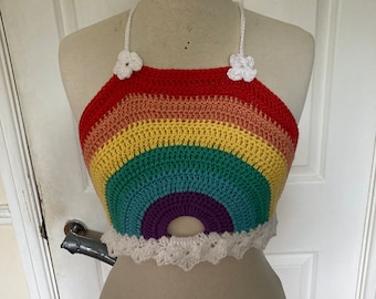 Puede incluir: Un top halter de crochet de arcoíris con flores de crochet blancas en las tiras y un ribete de crochet blanco alrededor de la parte inferior.