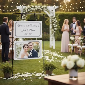 May include: A wedding sign with the text "Welcome to the Wedding of Josh [Names] 2021-2027" and a photo of a smiling couple. The sign is on a black metal stand, with a green lawn and guests in the background.